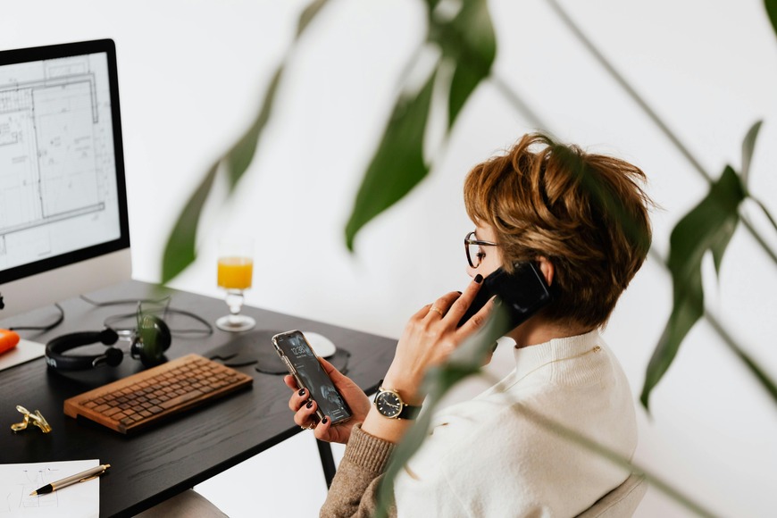 Woman in front of computer on the phone and looking at her smartphone.